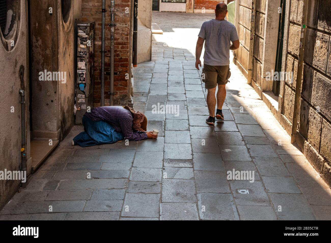 Turisti che camminano da donne che implorano per le strade di Venezia, Italia Foto Stock