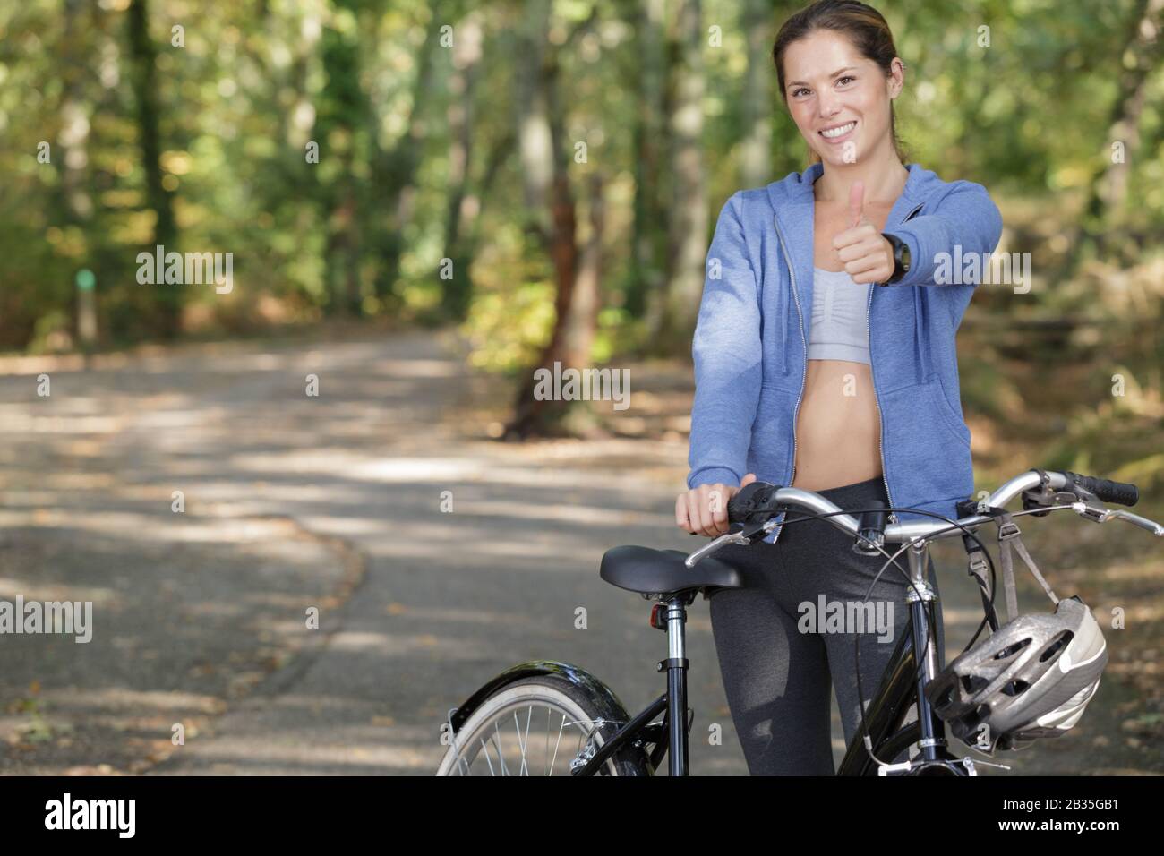 donna in bicicletta nella foresta che mostra pollice in su Foto Stock