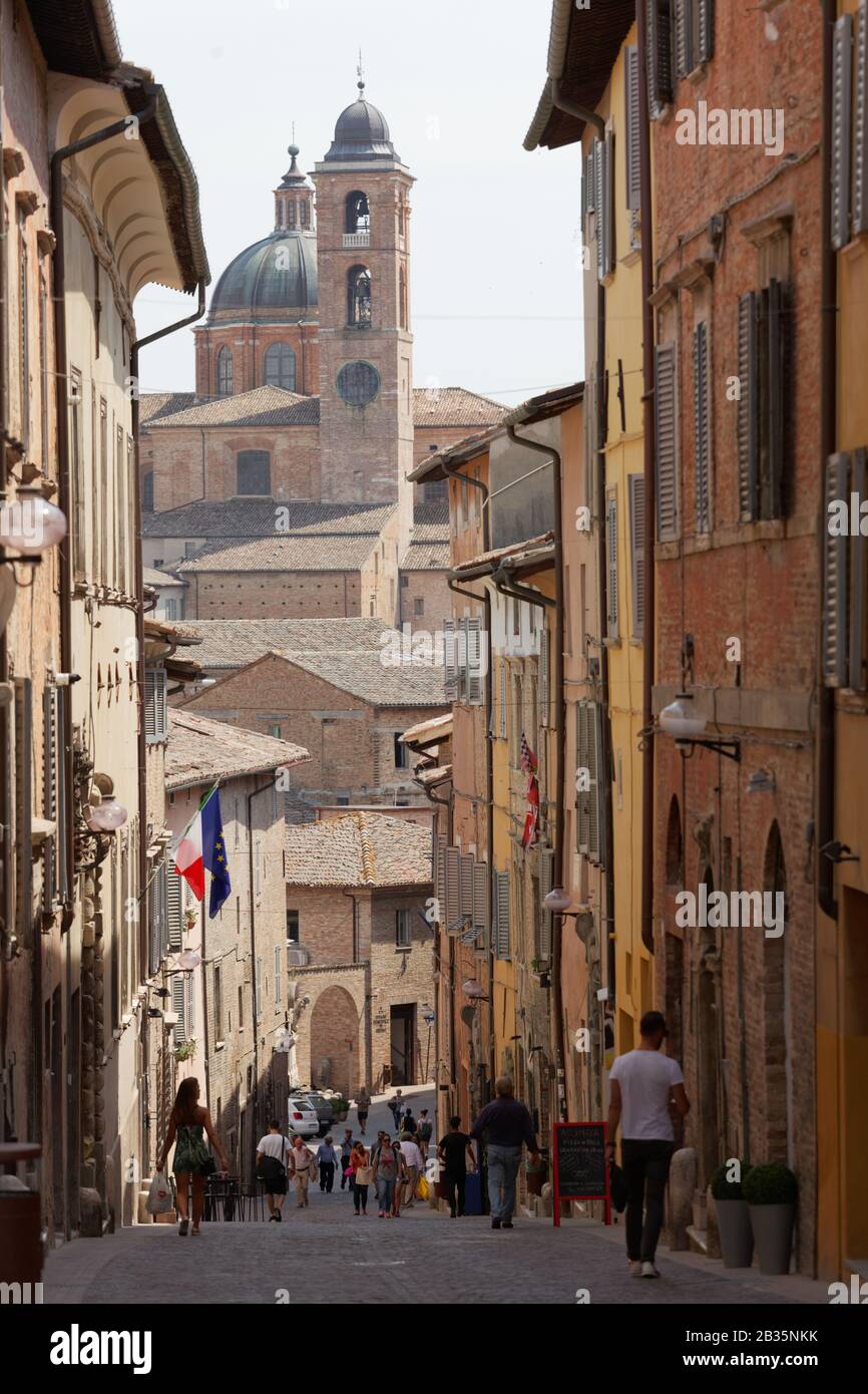 Turisti sulla stretta strada del centro storico di Urbino, Italia. La parte storica della città è dichiarata patrimonio dell'umanità dall'UNESCO Foto Stock