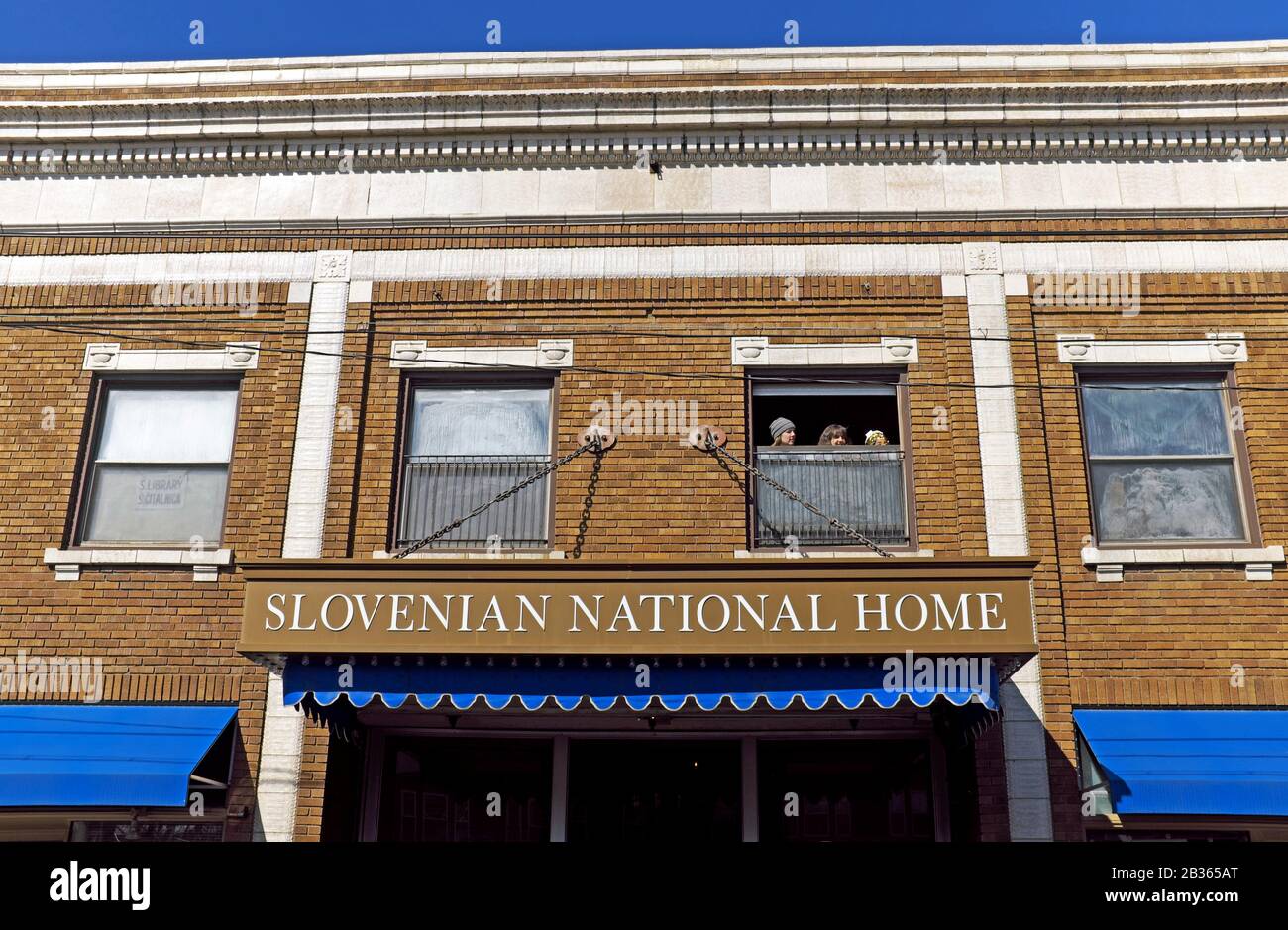 Tre donne guardano fuori la finestra sopra la casa nazionale slovena su St. Clair Avenue a Cleveland, Ohio, durante il Festival di Kurentovanje 2020. Foto Stock