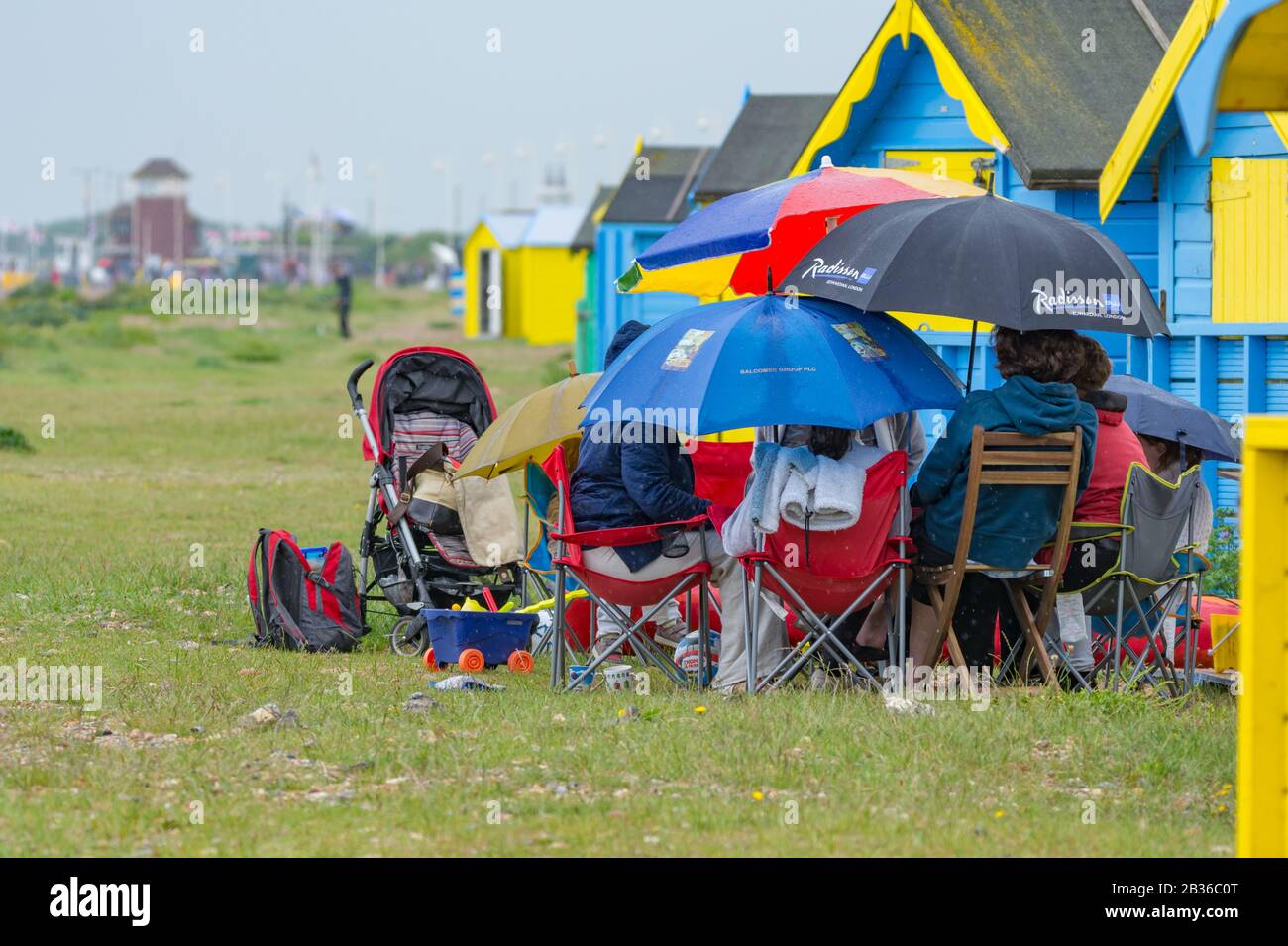 Persone seduti fuori sotto la pioggia su una spiaggia con ombrelloni, su un bagnato miserabile pioggia Bank Holiday Lunedi in una tipica giornata del tempo britannico, Regno Unito. Foto Stock