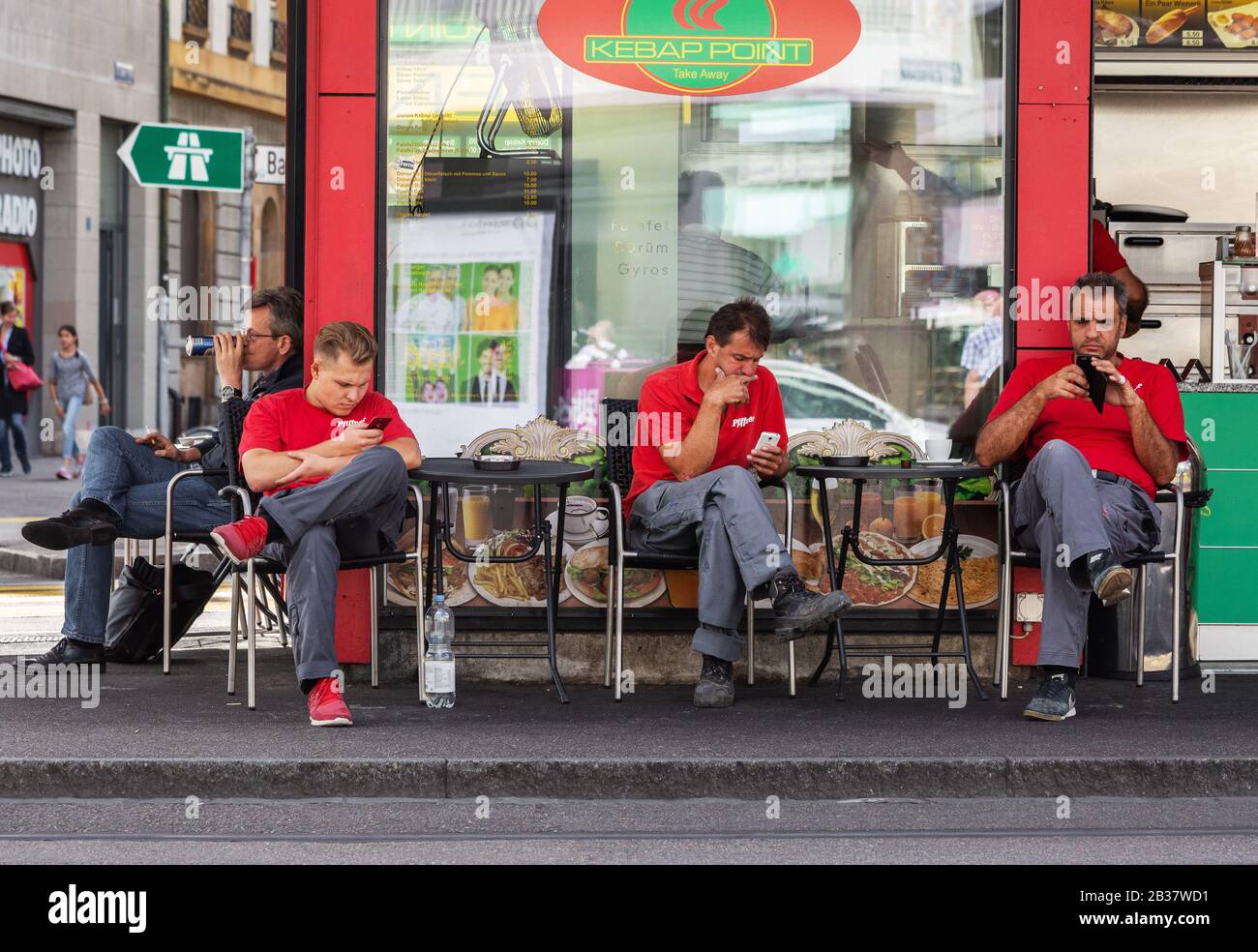 Gli uomini che usano il loro cellulare sedevano fuori da un bar in una strada a Basilea, Svizzera Foto Stock
