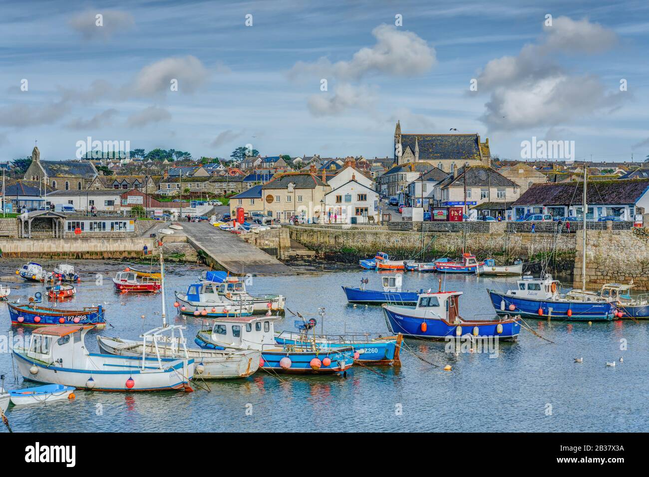 Nelle acque sicure del porto interno di Porthleven le barche da pesca sono allineate su di esso ormeggi con il vivace lato del mare e la città sullo sfondo. Foto Stock