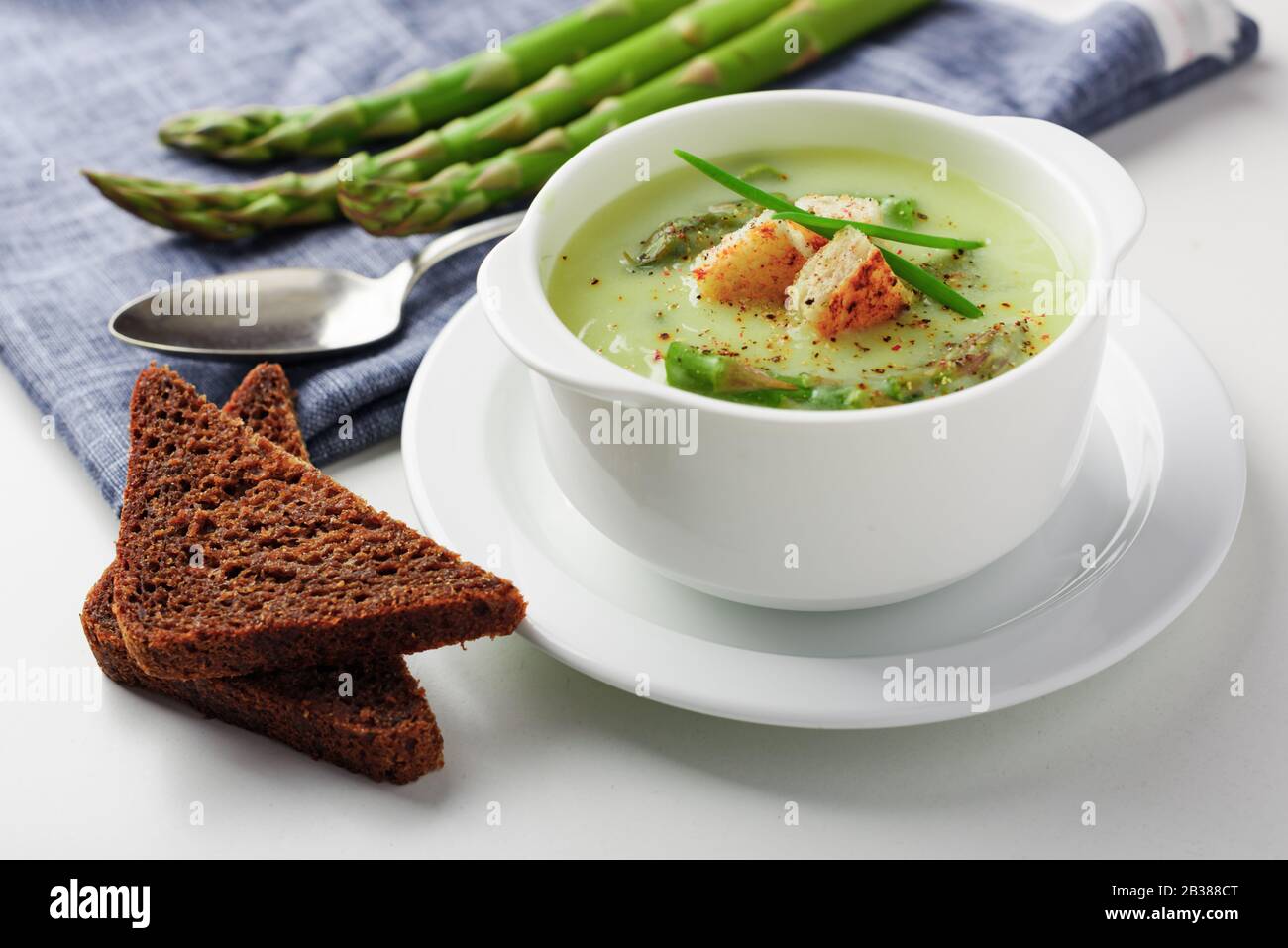 Zuppa di asparagi con pane nero in bianco ciotola closeup. Fotografia di cibo Foto Stock