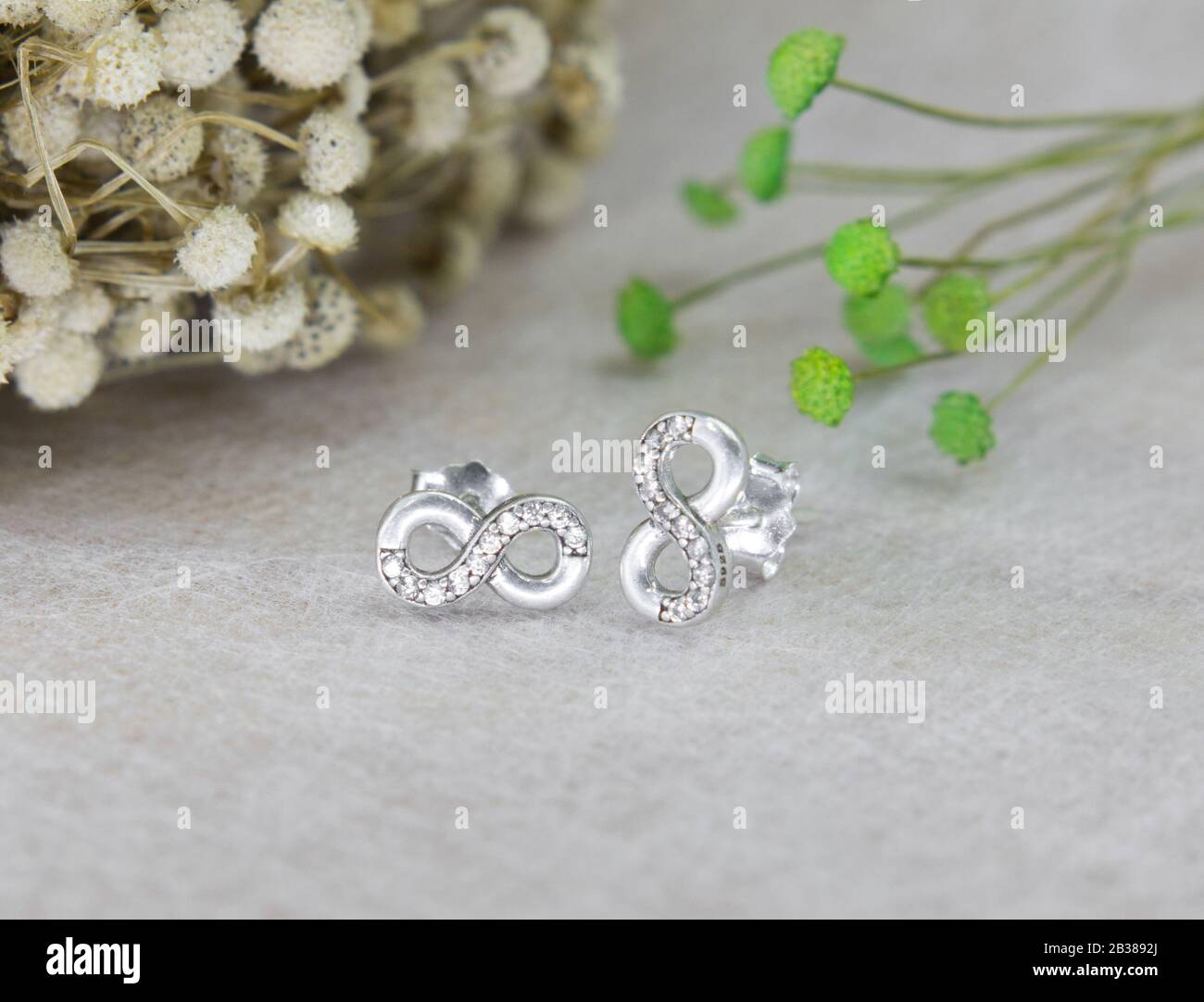 Un paio di splendidi orecchini a diamante a forma di infinito su sfondo grigio Foto Stock