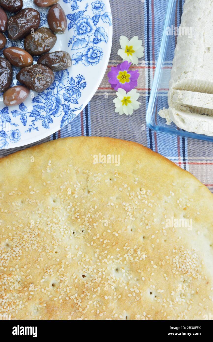 Flatbread, olive soleggiate su un piatto, halva di girasole e piccoli fiori di primula Foto Stock