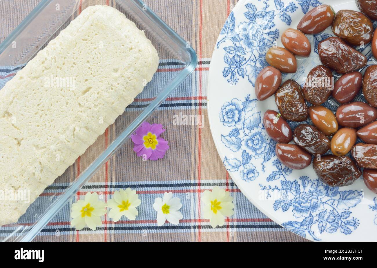 Olive secche al sole su un piatto, halva di girasole e piccoli fiori di primula Foto Stock
