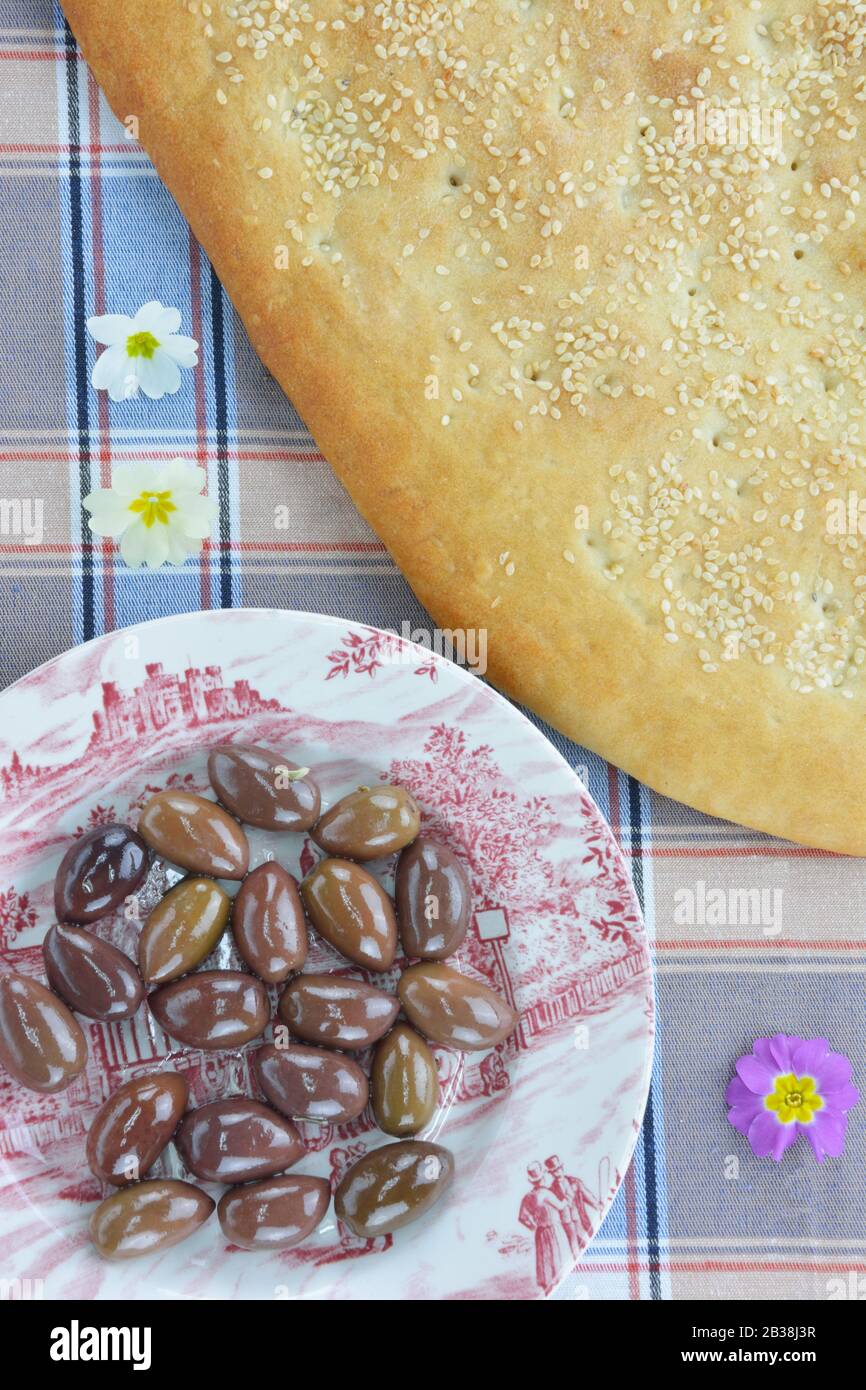 Flatbread, olive soleggiate su un piatto, halva di girasole e piccoli fiori di primula Foto Stock