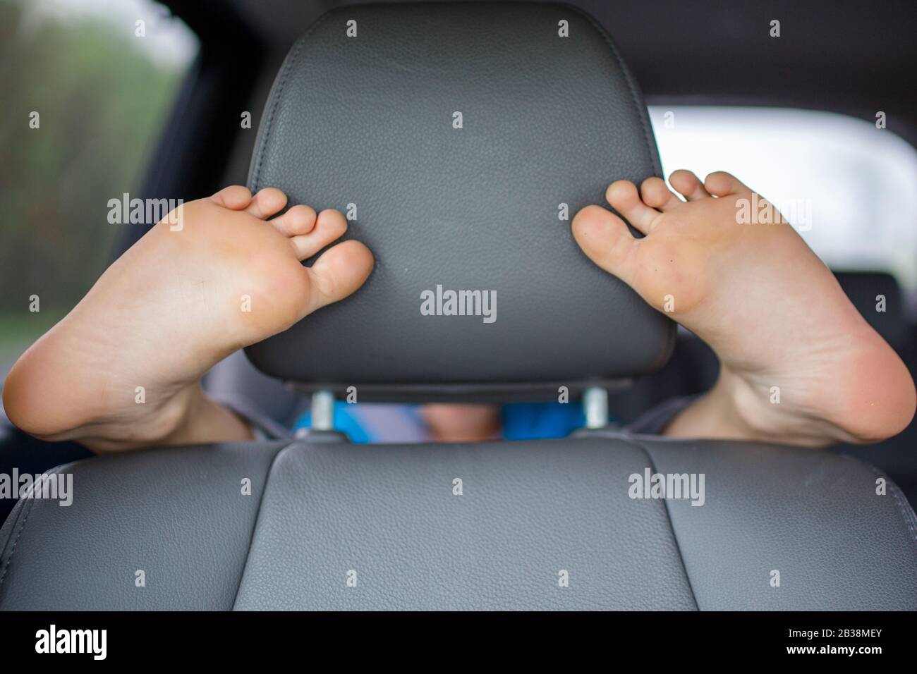 Un bambino seduto sul sedile posteriore di un'auto avvolge i piedi attorno al sedile anteriore Foto Stock