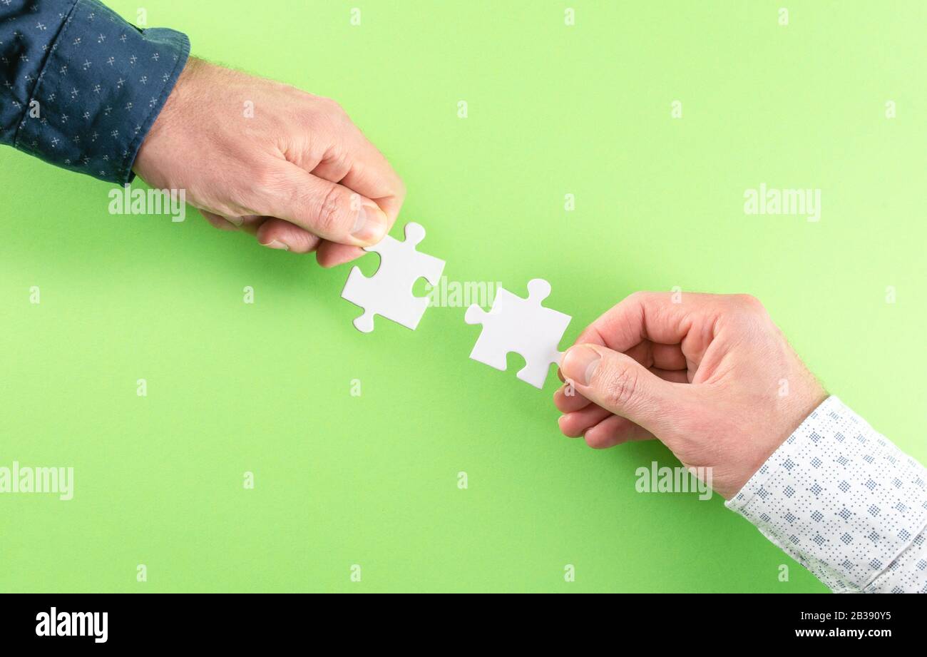 mani di due uomini d'affari che collegano pezzi di puzzle corrispondenti contro sfondo verde, partnership di affari e concetto di lavoro di squadra Foto Stock