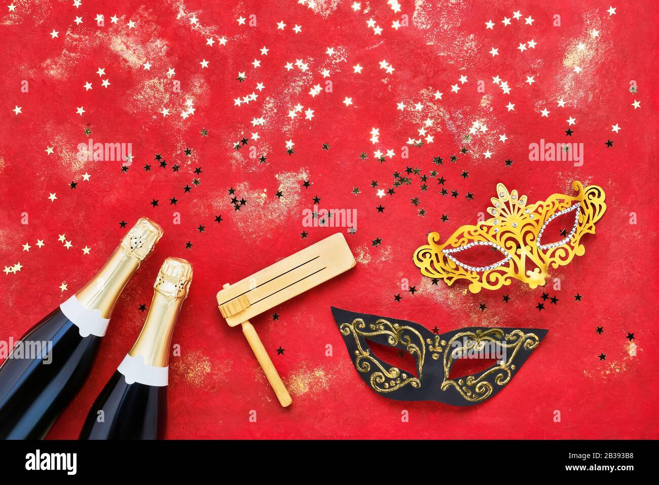 Due bottiglie di champagne, maschera di carnevale e gragger su sfondo rosso. Piatto di Natale, Capodanno, Purim, celebrazione del Carnevale concetto. Foto Stock