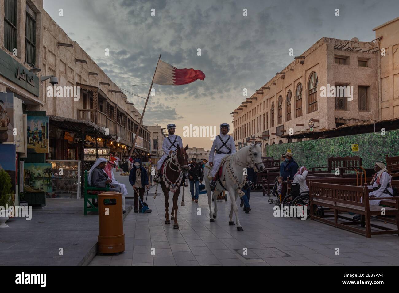 Souk Waqif Doha, Qatar principale strada vista di luce del giorno con tradizionale polizia equitazione cavalli e bandiera Qatari in background Foto Stock
