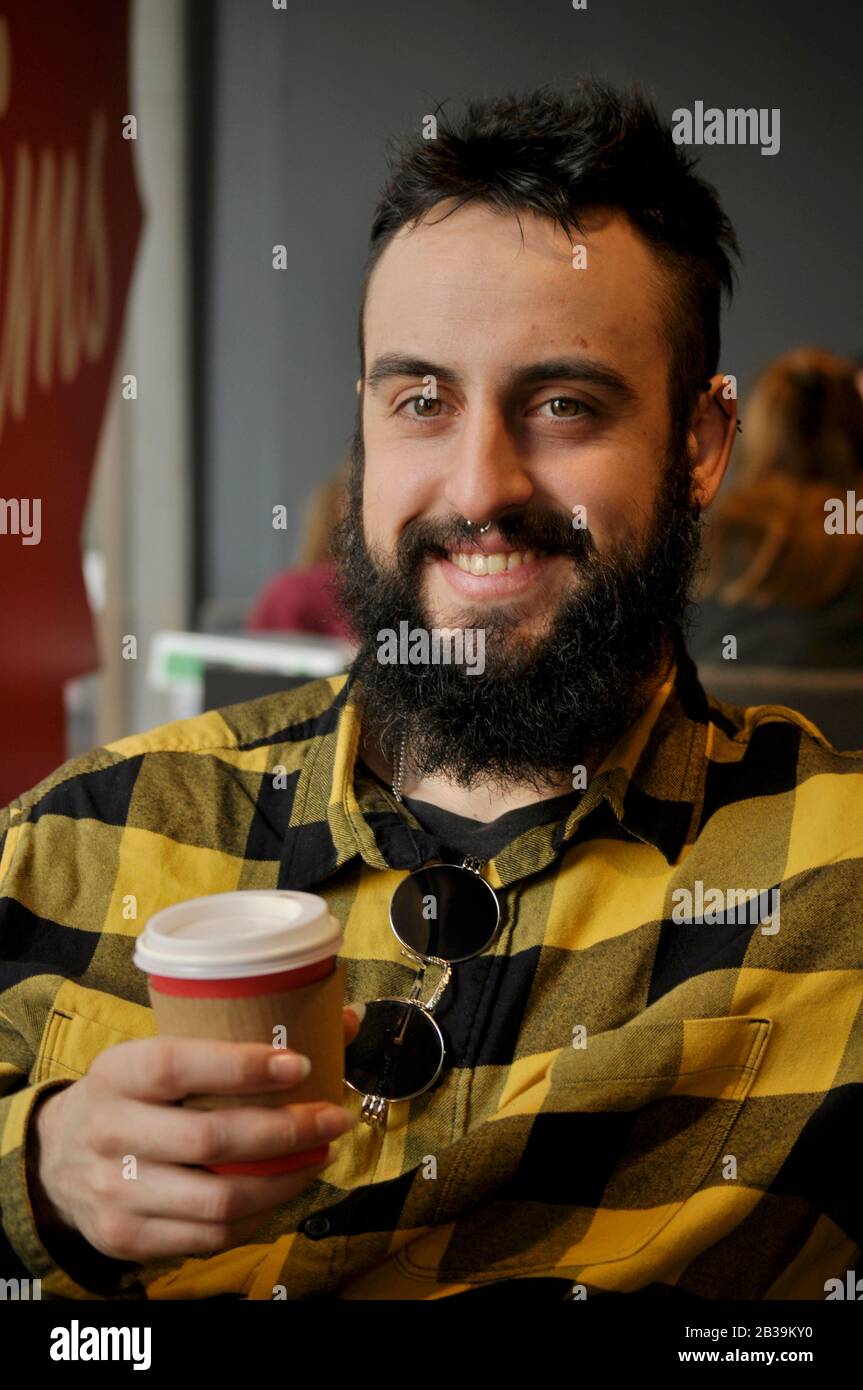 Giovane uomo che beve caffè in una caffetteria presto la mattina/ avere un grande sorriso Foto Stock