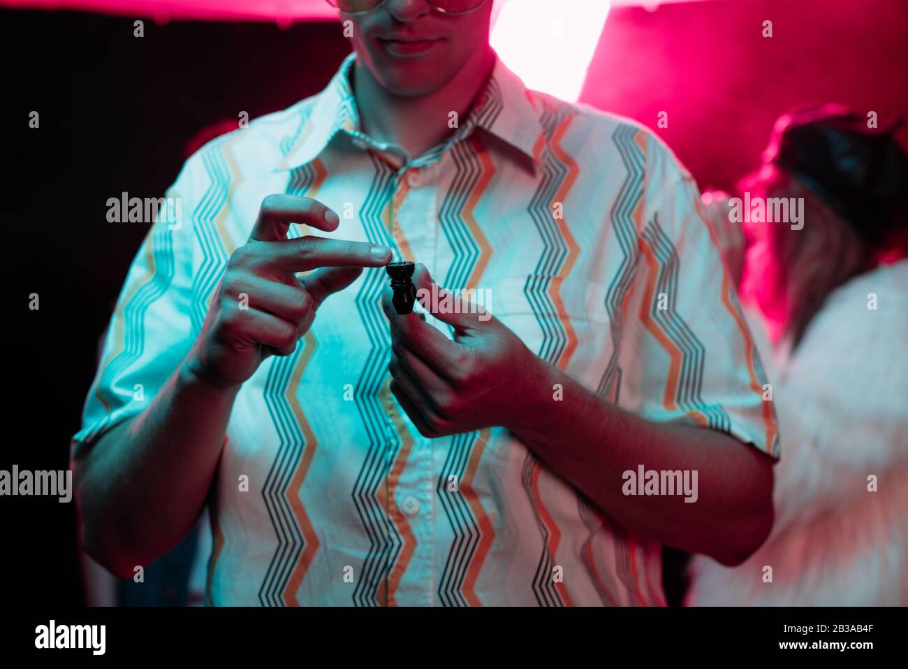Vista ritagliata dell'uomo che tiene la pipa fumante con marijuana in discoteca Foto Stock
