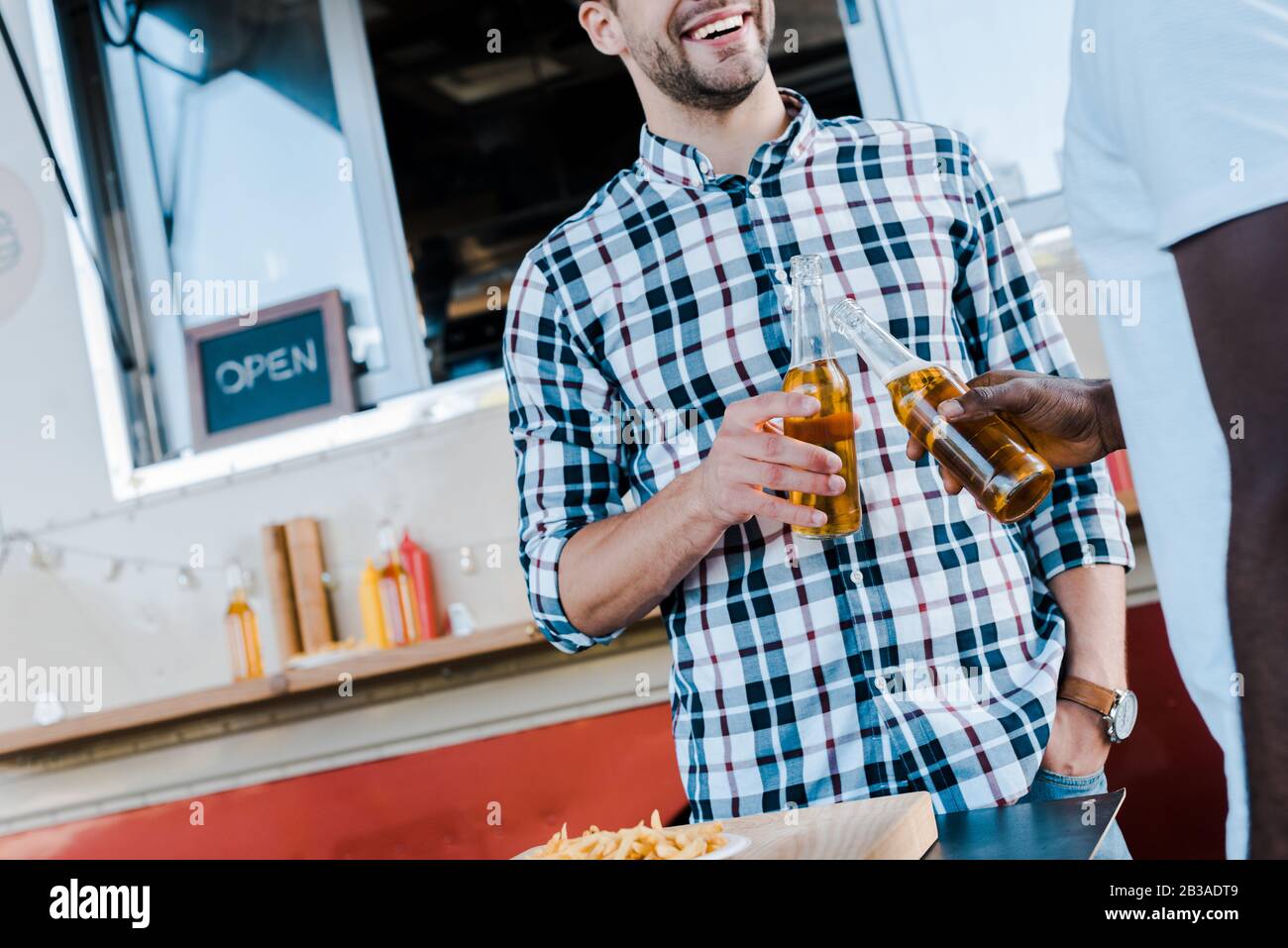 vista corta di uomini multiculturali felici tostare bottiglie di birra Foto Stock