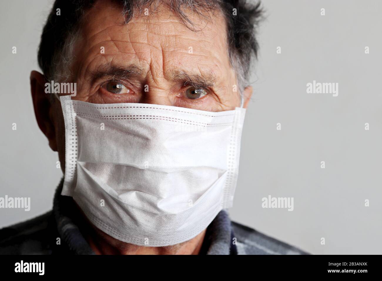 L'uomo anziano nella maschera medica sembra sconvolto. Concetto di protezione contro il coronavirus, malattia, febbre, raffreddore e influenza Foto Stock