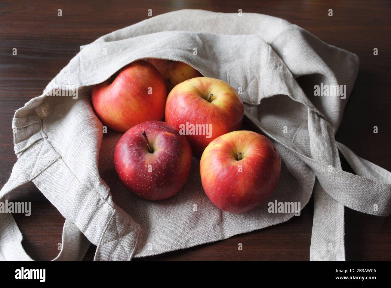 Vista del gruppo di mele rosse, fresche, biologiche, colorate, con un sacchetto di colore neutro in lino su tavolo in compensato scuro in luce naturale Foto Stock