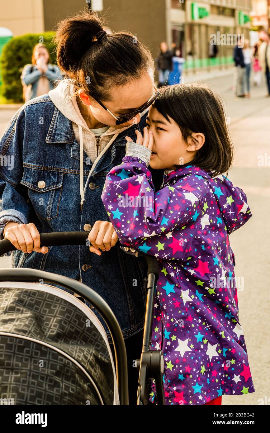 Saint-Lambert, Canada - 26 maggio 2019: La figlia sussurra a sua madre che sta spingendo un trasporto del bambino Foto Stock