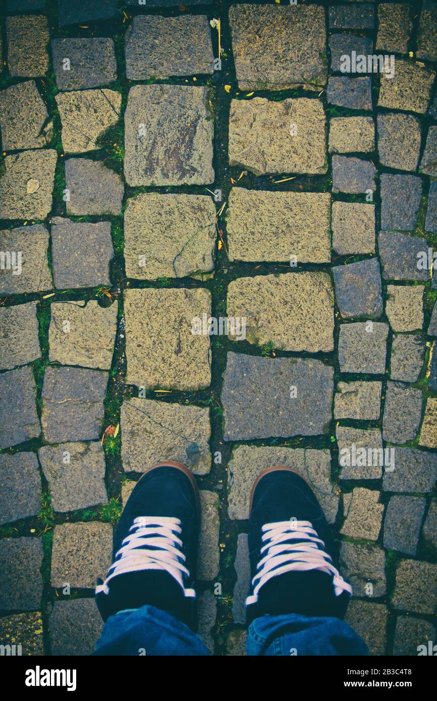 Vista dall'alto dei piedi in un paio di sneaker skater su un pavimento in ciottoli. Sfondo a motivi di ciottoli. Stile urbano minimalista. Foto Stock
