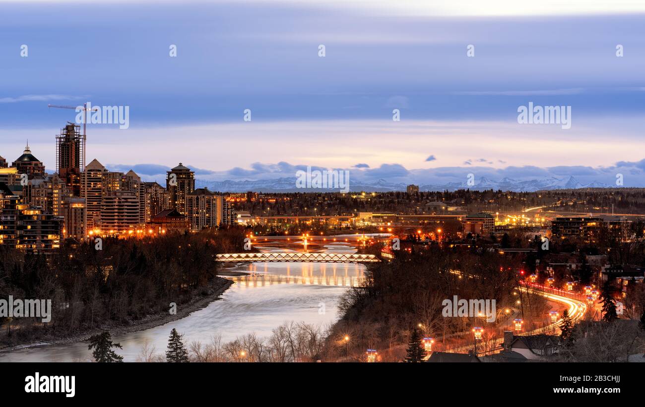 Calgary di notte, Alberta, Canada. Peace Bridge sul fiume Bow di notte, Calgary centro di notte autunno con il fiume in primo piano e le montagne in ba Foto Stock