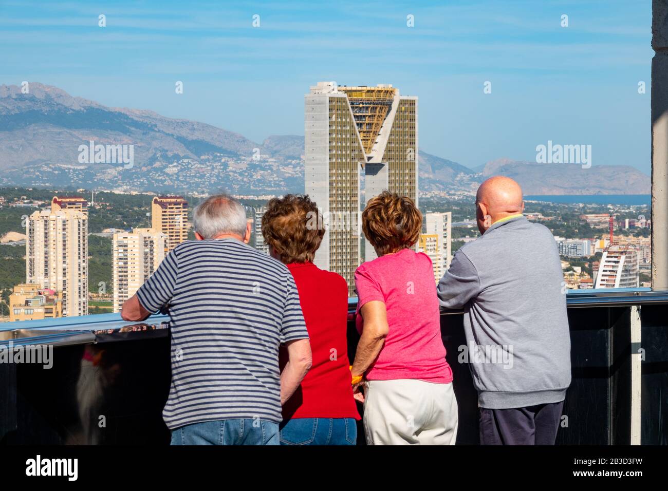 Due coppie anziane guardano l'alto complesso residenziale di appartamenti Intempo al sole con le sue montagne sullo sfondo, Benidorm, Spagna, Europa. Foto Stock