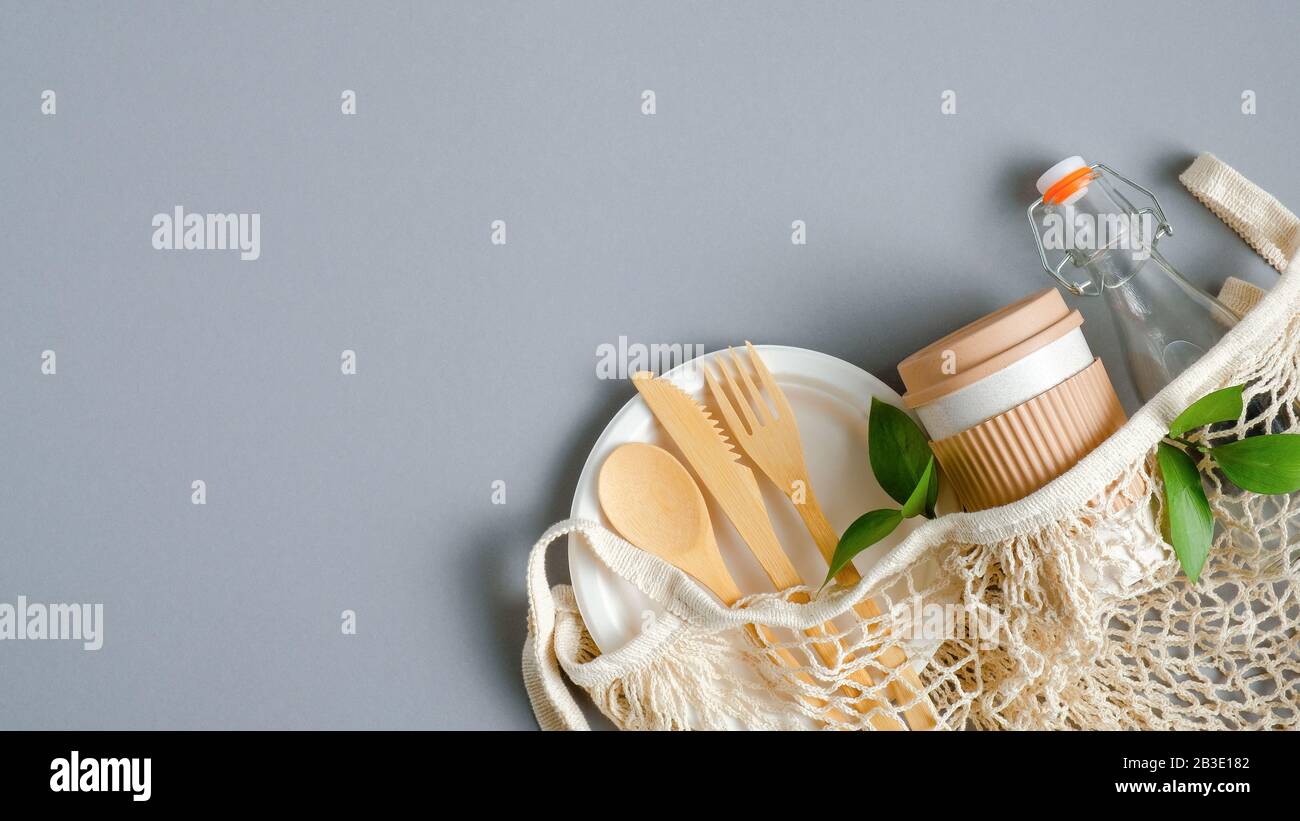 Set di posate da viaggio eco-friendly, tazza e bottiglia in sacchetto in mesh su sfondo grigio. Zero rifiuti, concetto senza plastica. Stile di vita sostenibile Foto Stock