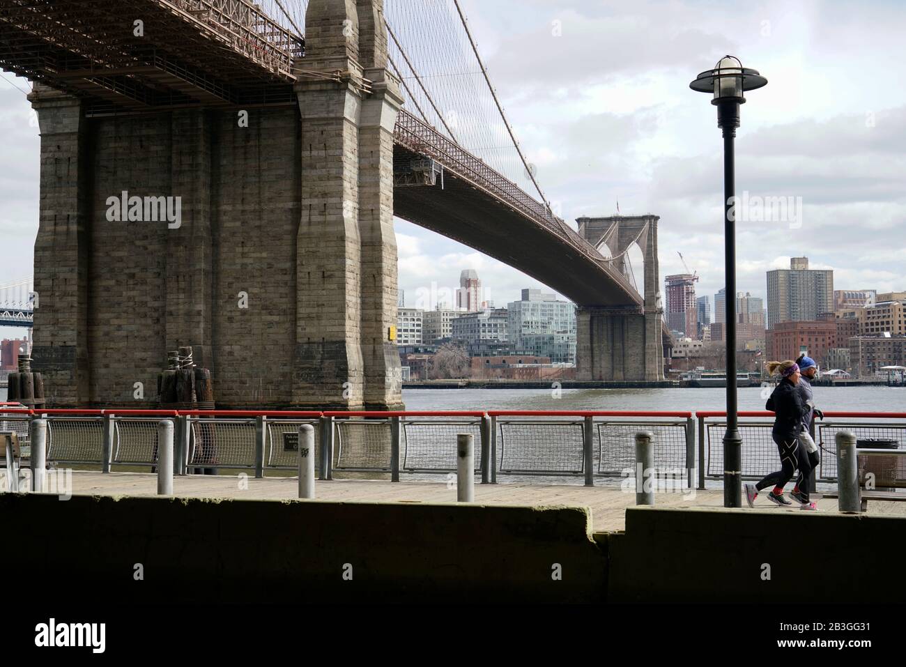Ponte di Brooklyn sull'East River con joggers in esecuzione su East Fiume Greenway sul lato di Manhattan e skyline di Brooklyn in The background.Lower Manhattan.New York City.USA Foto Stock