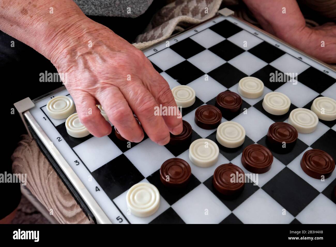 La mano di una vecchia nonna muove gli ispettori attraverso il campo di gioco. Dama Marrone E Bianca. Foto Stock