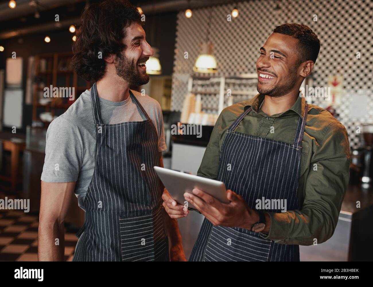 Colleghi di sesso maschile allegri che usano un tablet digitale sul bancone della caffetteria e ridono Foto Stock