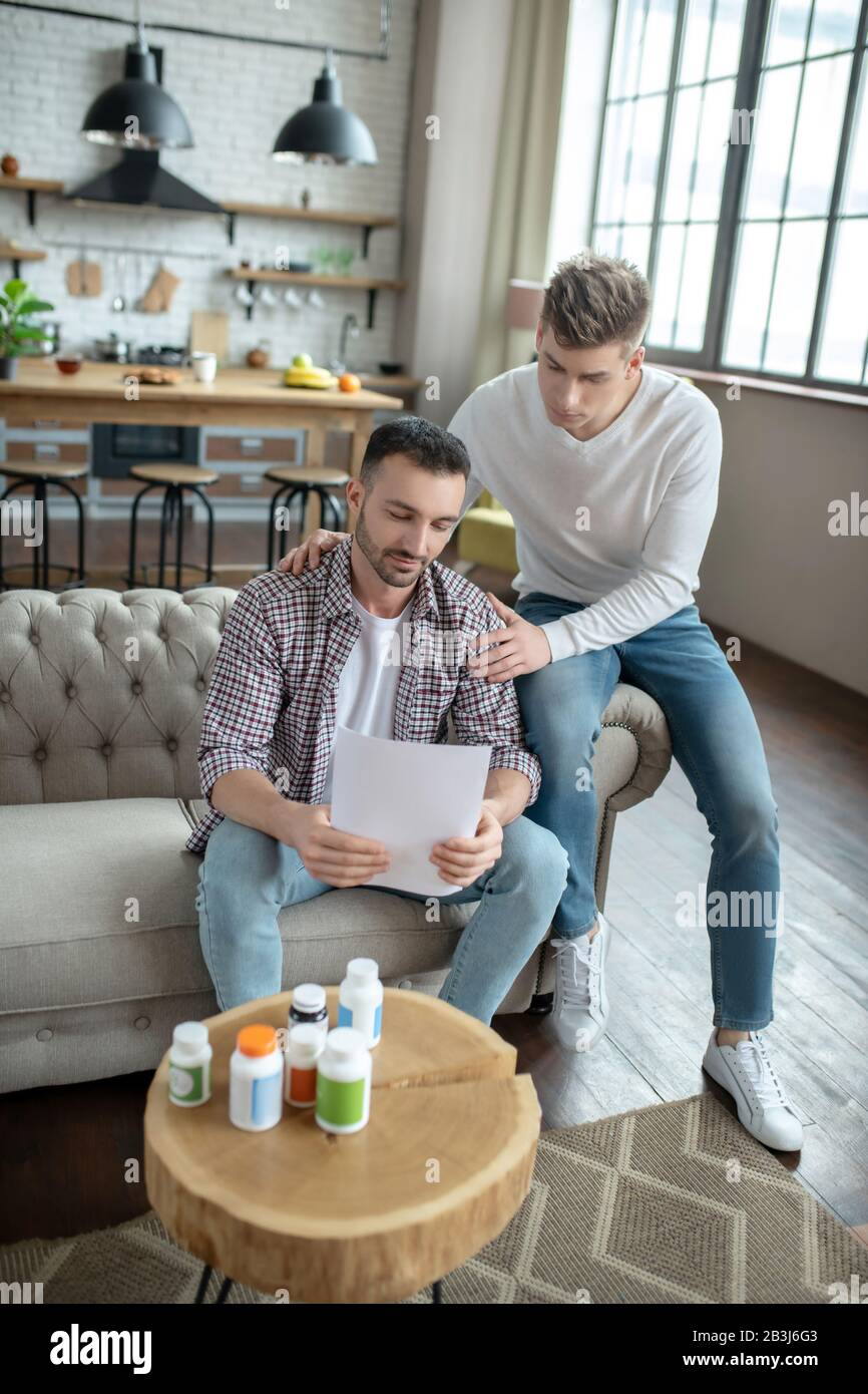 Giovane uomo bearded in una camicia a scacchi sentendosi infelice mentre legge i risultati della prova Foto Stock