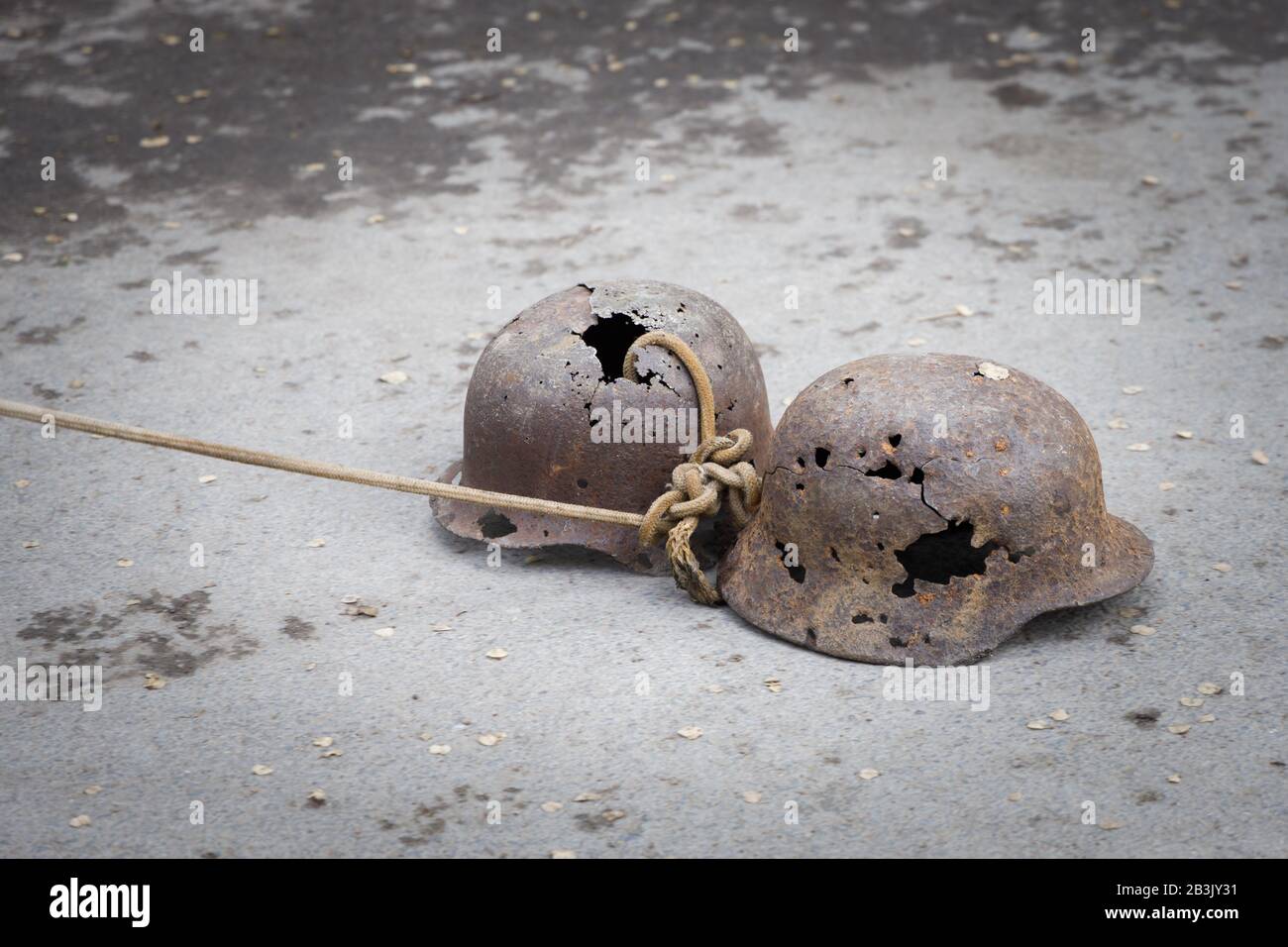 Due caschi militari tedeschi perforati con proiettili tirare su una corda su asfalto come simbolo di vittoria sugli invasori nazisti. Foto Stock