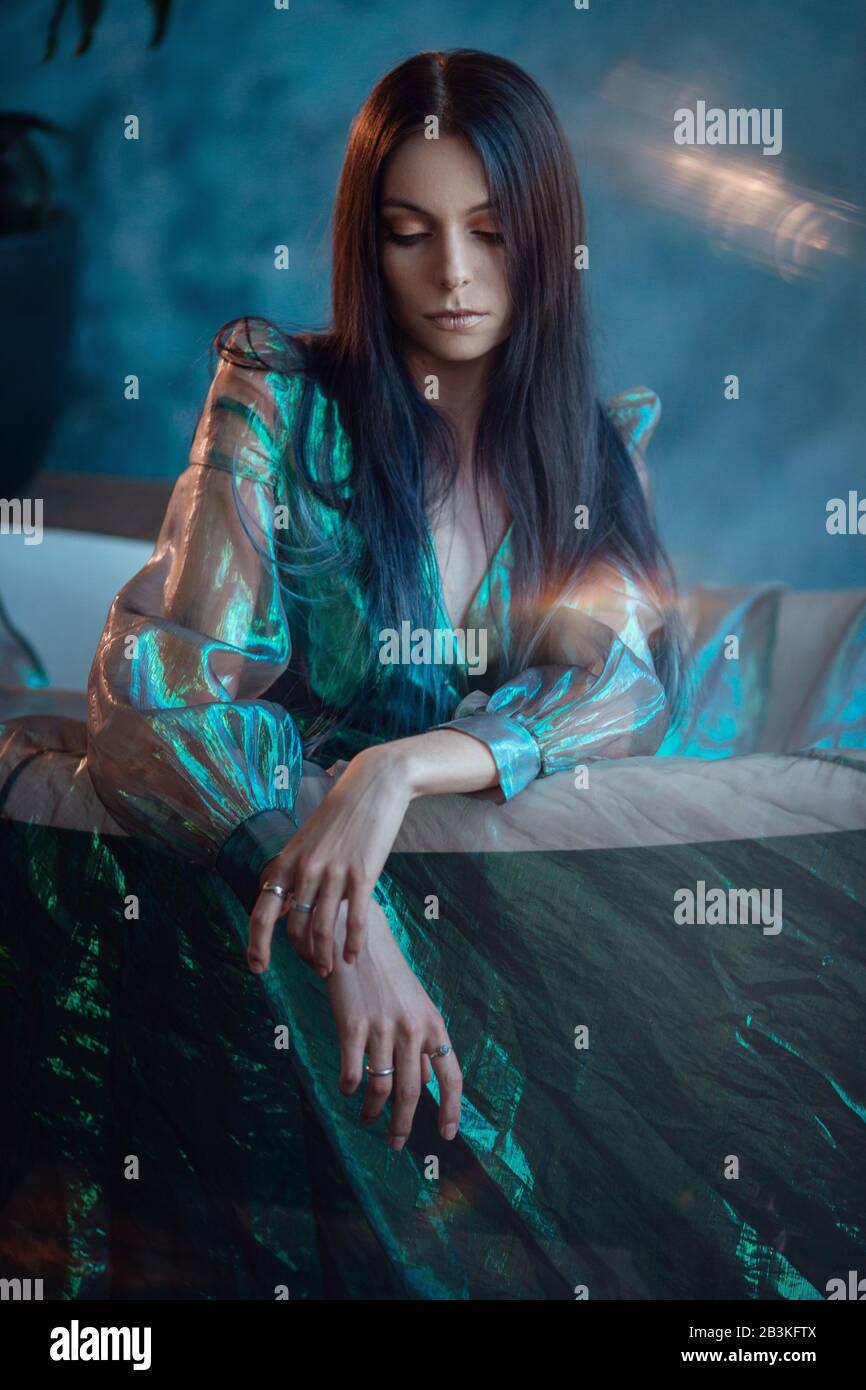 Una donna assomiglia ad una piccola sirena triste da una fiaba. Bella sposa rilassante nella vasca. Abito da sposa colori Serenity White Studio. Foto Stock