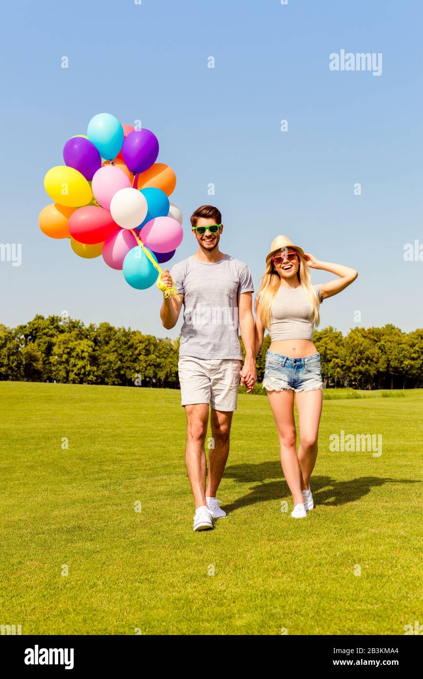 Felice giovane coppia nell'amore che tiene i palloncini e cammina insieme sull'erba verde Foto Stock