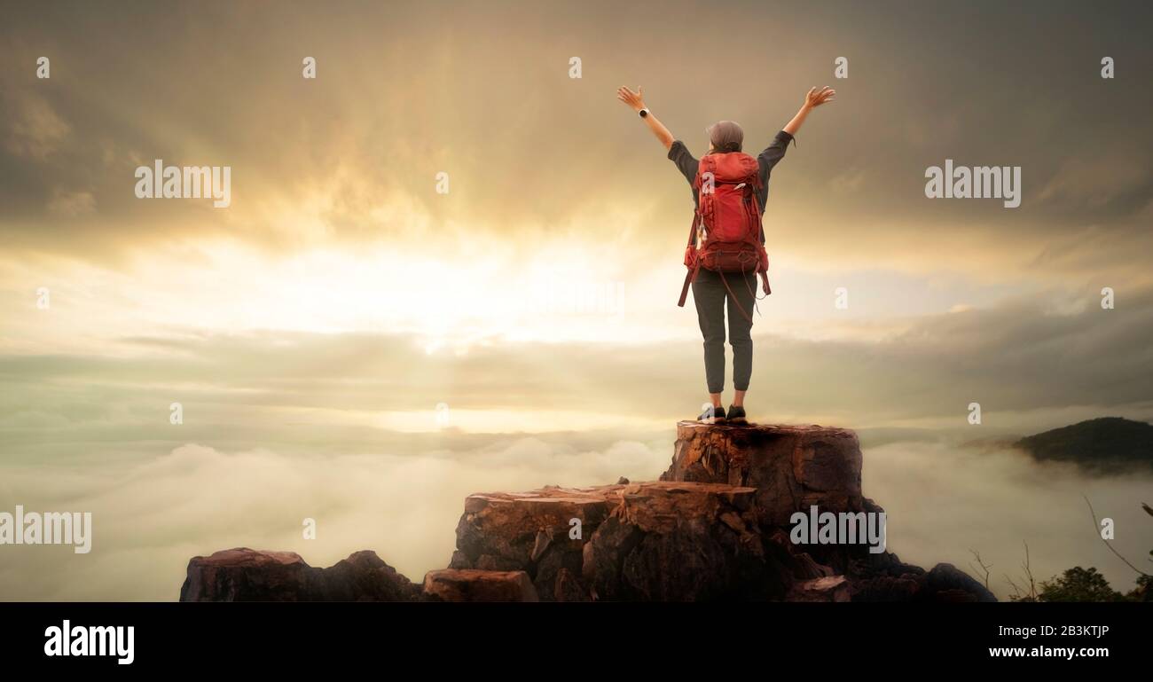 Backpacker donna sollevare mano sulla cima della montagna con il cielo sole e nebbia backgeound Foto Stock