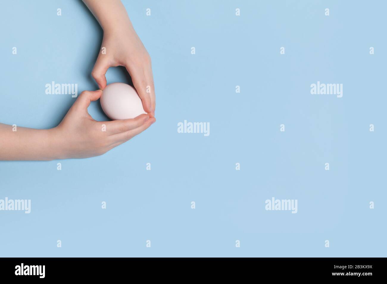 Uovo di pollo bianco nelle mani di un bambino su uno sfondo blu. Concetto di Pasqua con gesto di forma cardiaca Foto Stock