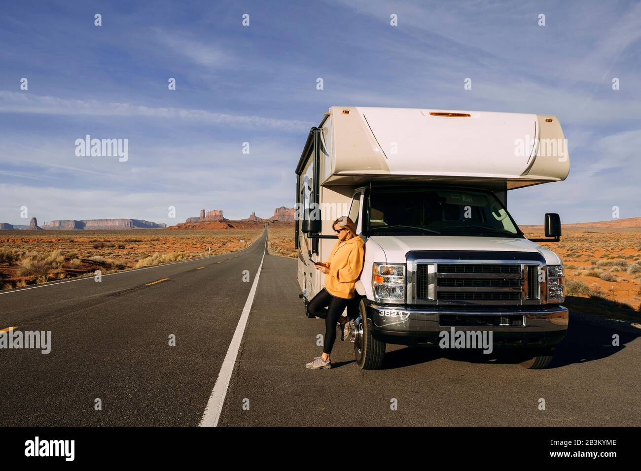 Una donna viaggia in camper attraverso la Monument Valley nel deserto degli Stati Uniti e controlla il suo telefono cellulare parcheggiato sul lato della strada Foto Stock