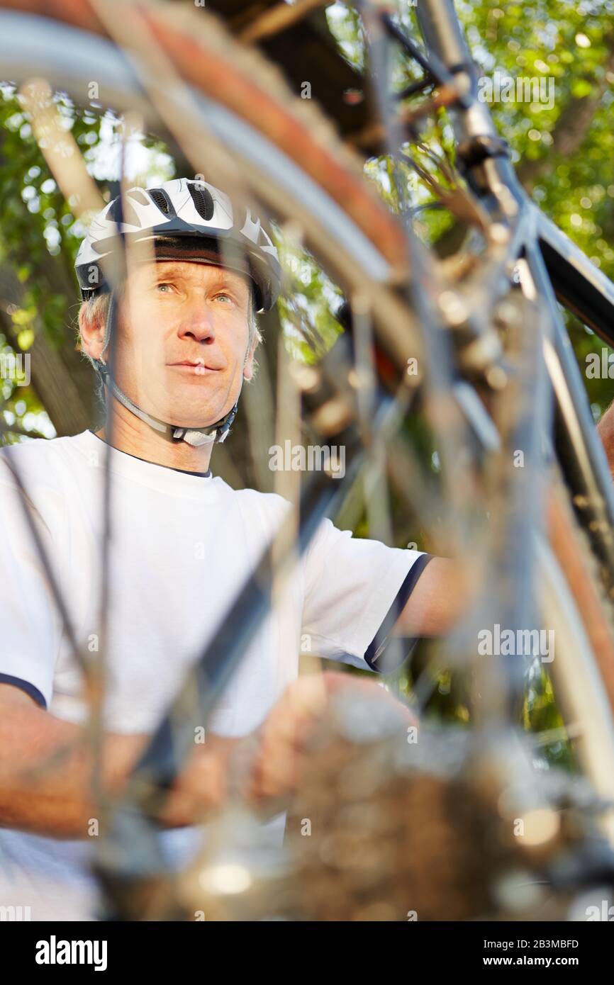 Uomo con casco da bicicletta mentre ripara la sua bicicletta Foto Stock