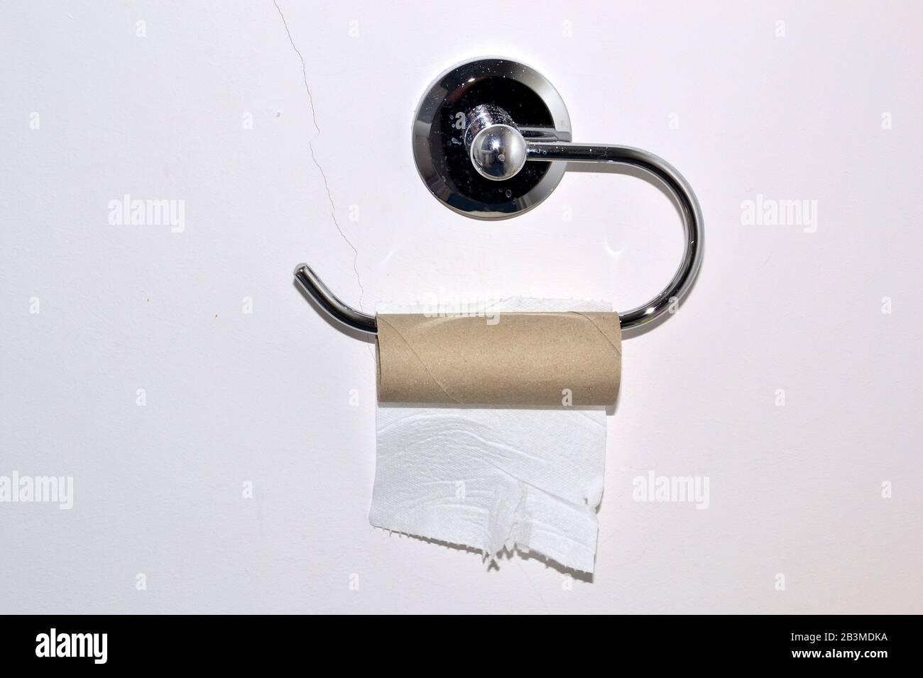 L'ultimo foglio di rotolo di carta igienica su un supporto per rotolo di carta igienica quasi vuoto su una parete di gabinetto o di toilette Foto Stock