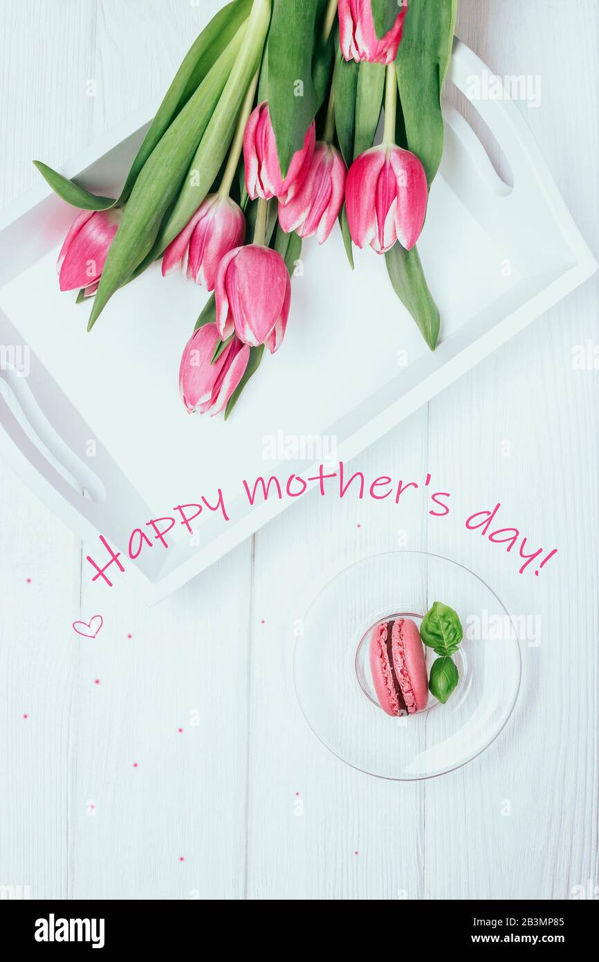 Biglietto di auguri di buon giorno per la madre. Tulipani di primavera rosa e macaron di lampone su sfondo bianco. Vista dall'alto Foto Stock