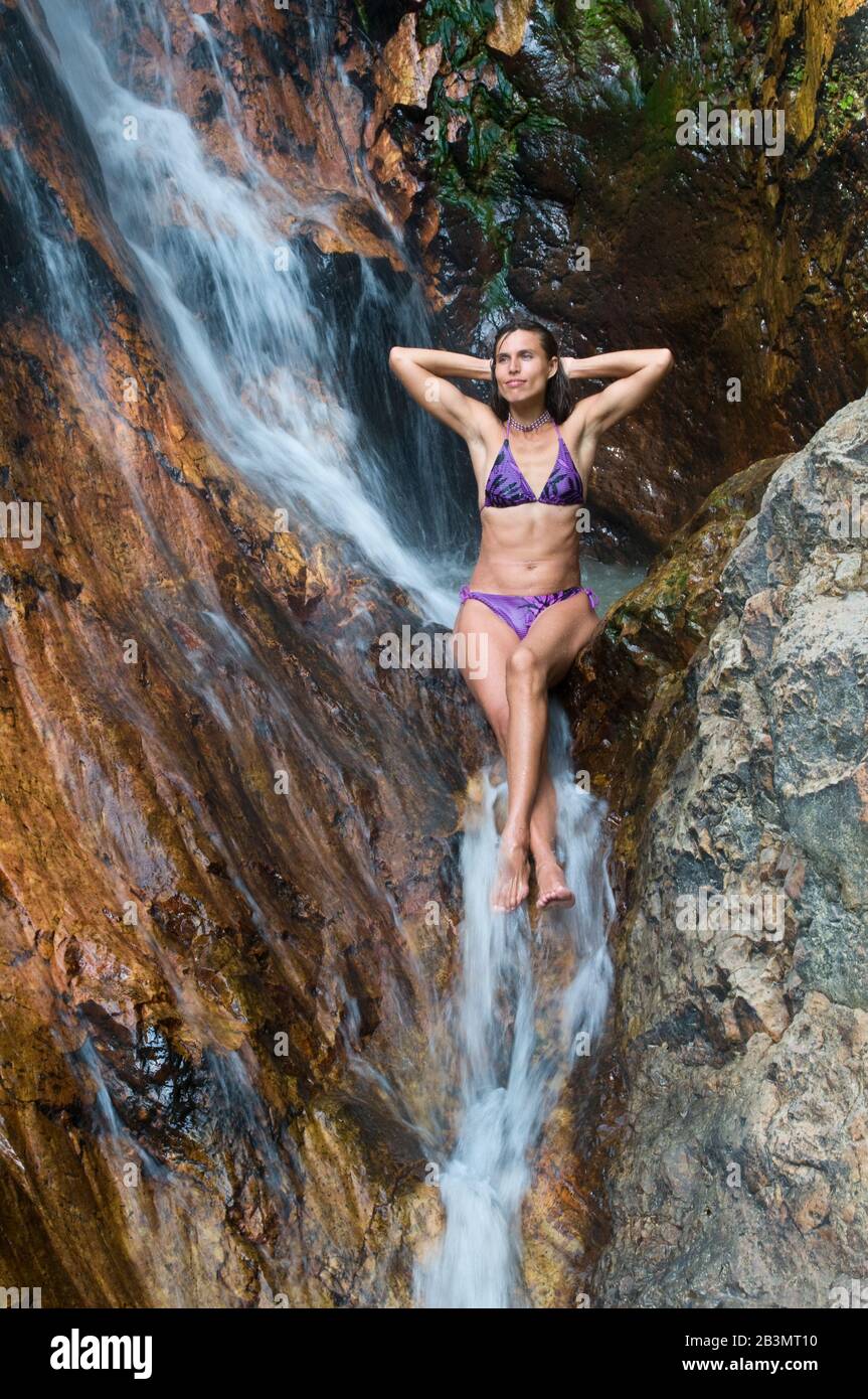 La donna prende piacere nel fare il bagno nella cascata. La giovane donna è vestita con costume da bagno a due pezzi viola. Foto Stock