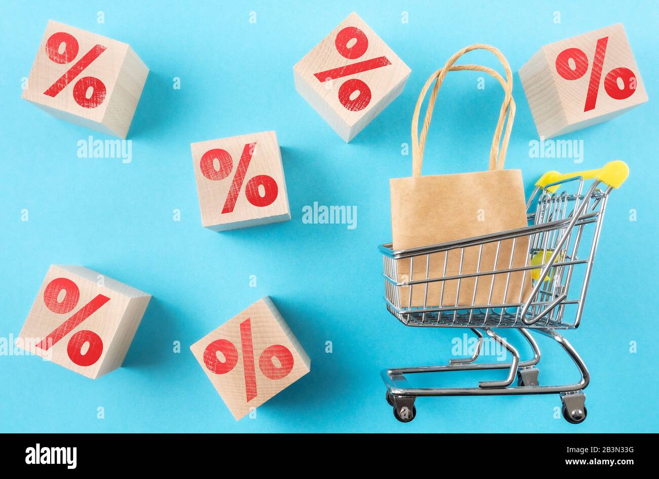 carrello con shopping bag e segno rosso per cento su cubi di legno su sfondo blu, vendita al dettaglio e concetto di sconto Foto Stock