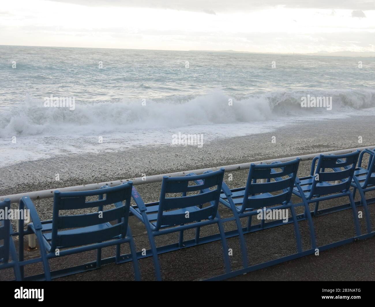 Una fila di sedie a sdraio blu in metallo che si affacciano sui mari tempestosi sulla Promenade des Anglais a Nizza, marzo 2020 Foto Stock