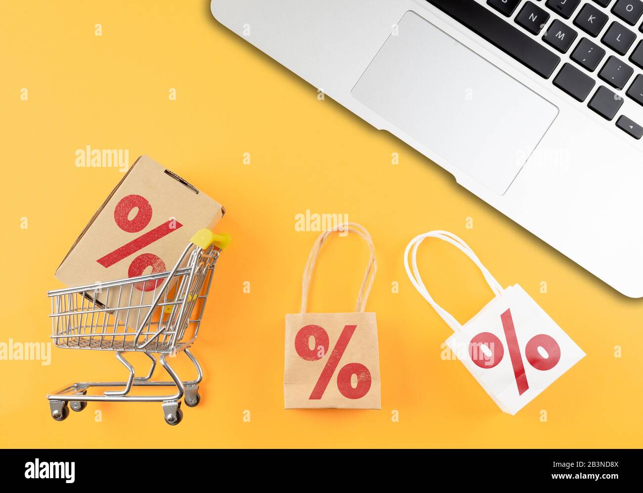 acquisto online e concetto di e-commerce con carrello e computer portatile su scrivania arancione Foto Stock