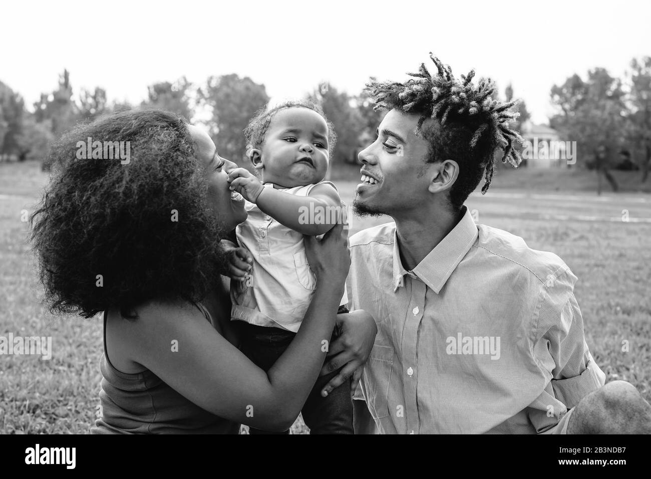 Felice famiglia africana godendo di un momento tenera durante il fine settimana all'aperto - madre e padre divertirsi con la loro figlia in un parco pubblico Foto Stock