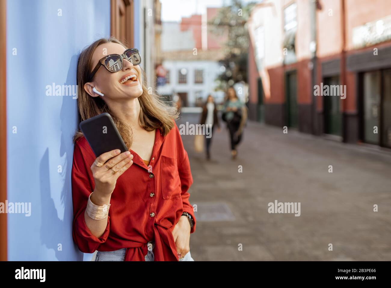 Ritratto di Lifetyle di una donna elegante che ascolta la musica con telefono e cuffie senza fili in piedi rilassato sulla strada nella città vecchia Foto Stock