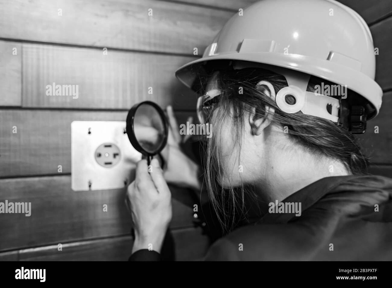 fuoco selettivo sulla mano della donna dell'ispettore di costruzione che tiene una lente d'ingrandimento per osservare da vicino la presa di elettricità di 220v per asciugatore di vestiti Foto Stock