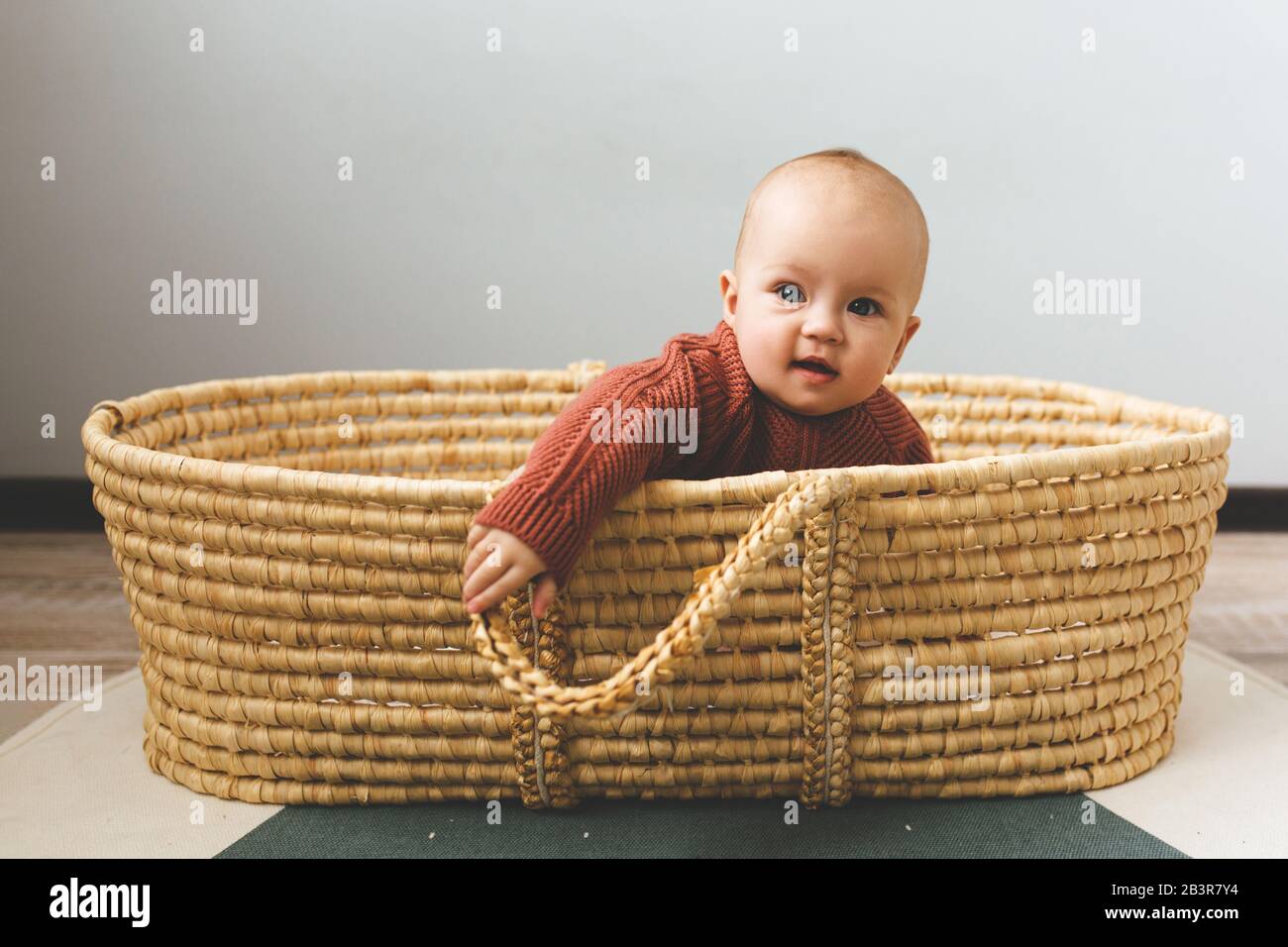 Adorabile bambina di sei mesi in un cesto sul pavimento e guardando nella macchina fotografica Foto Stock