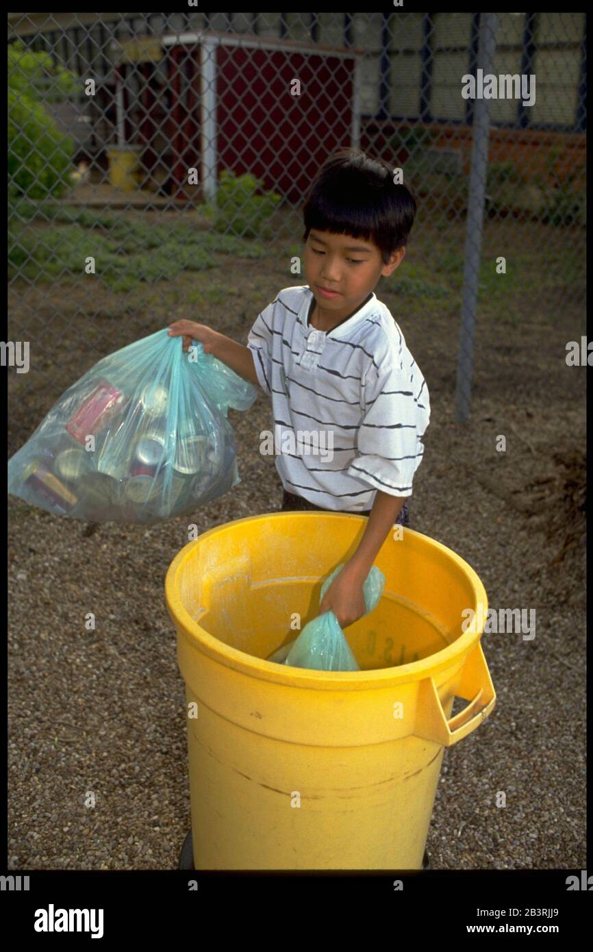 Austin Texas USA: Il ragazzo coreano-americano mette i sacchetti riempiti di spazzatura che ha preso sui terreni della scuola in un cestino di plastica. ©Bob Daemmrich Foto Stock
