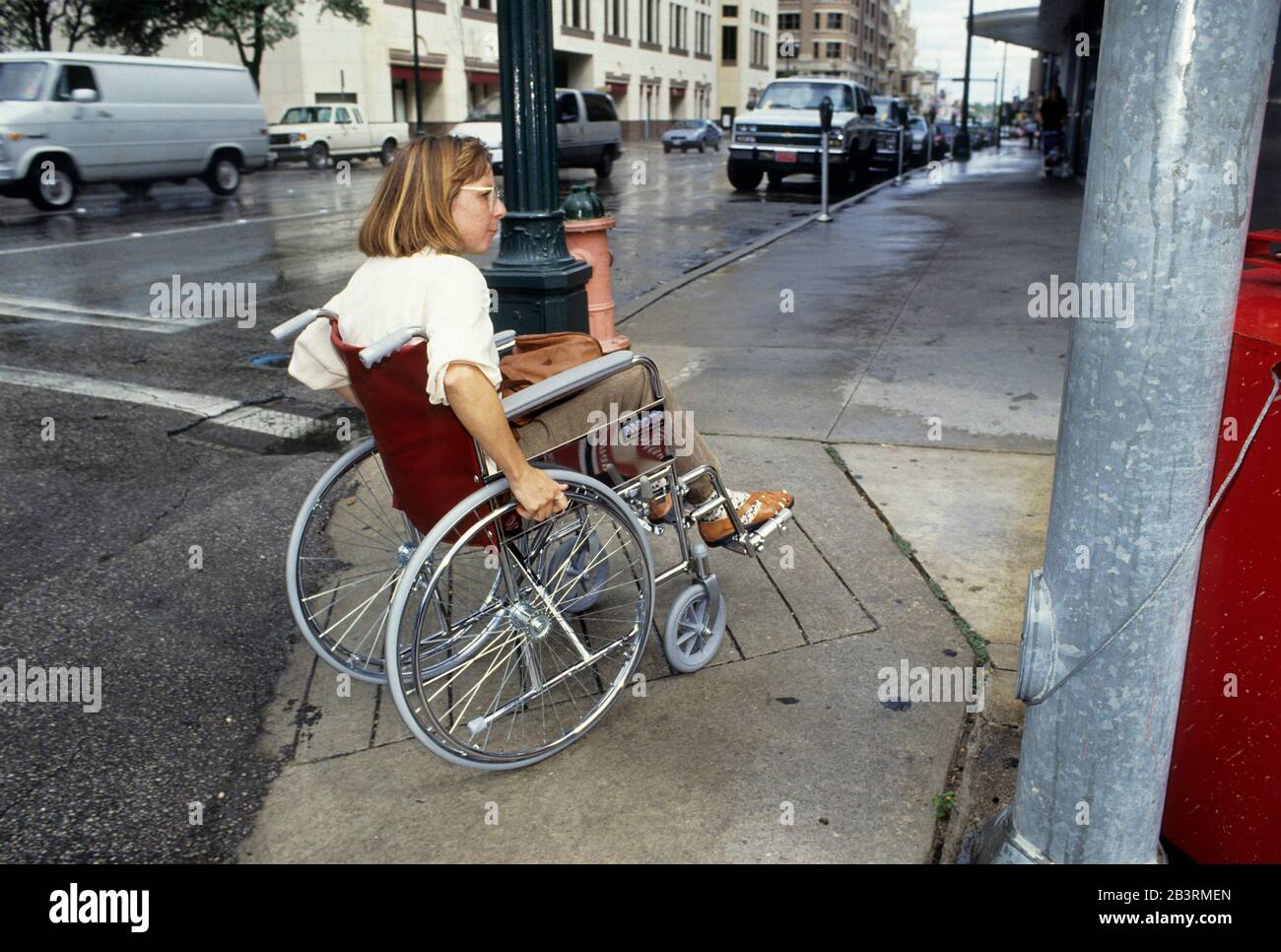 Austin, Texas USA: La donna handicappata in sedia a rotelle utilizza il taglio del marciapiede e la rampa sul marciapiede accessibile ai disabili nel centro città. ©Bob Daemmrich Foto Stock