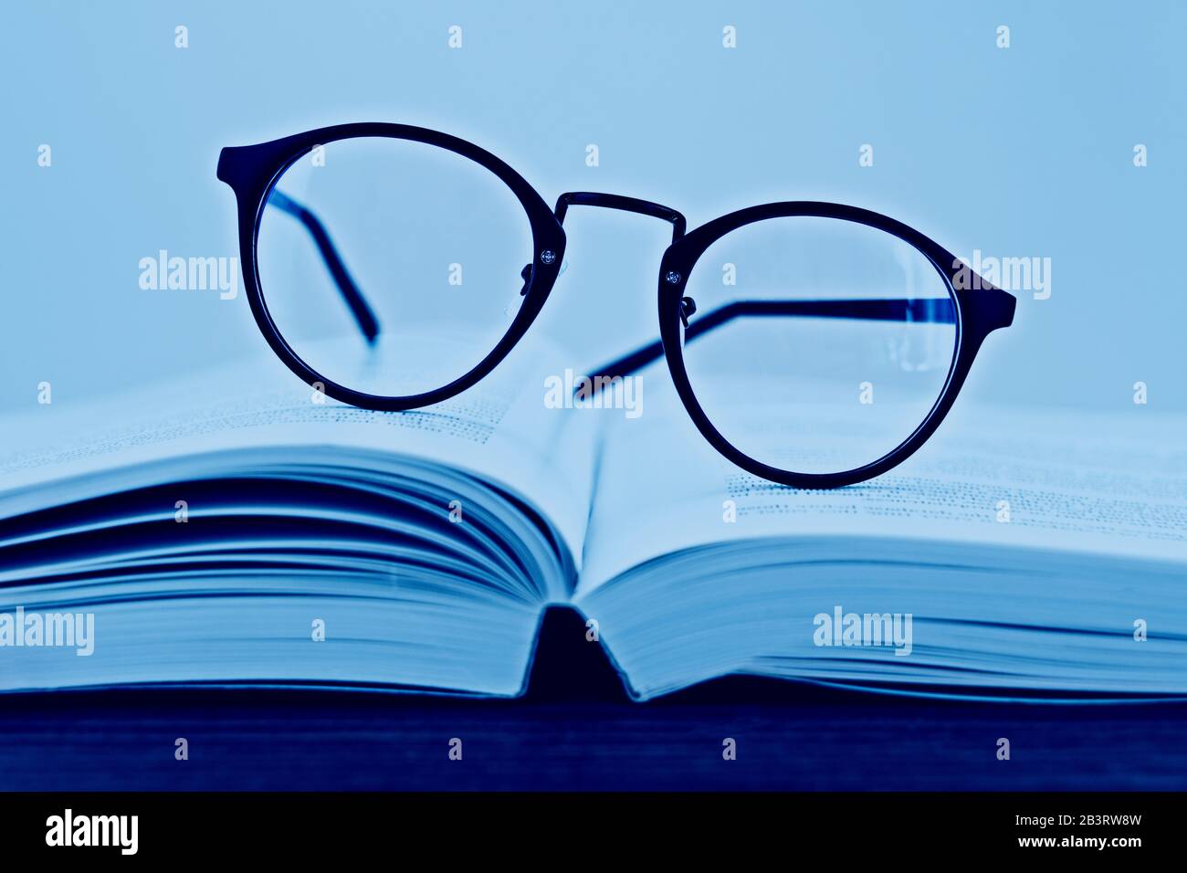 Occhiali da lettura hippster su un libro aperto con spazio di copia. Immagine classica con tonalità blu. Il giorno del libro mondiale è il 23 aprile. Profondità Di Campo bassa e fo selettivo Foto Stock